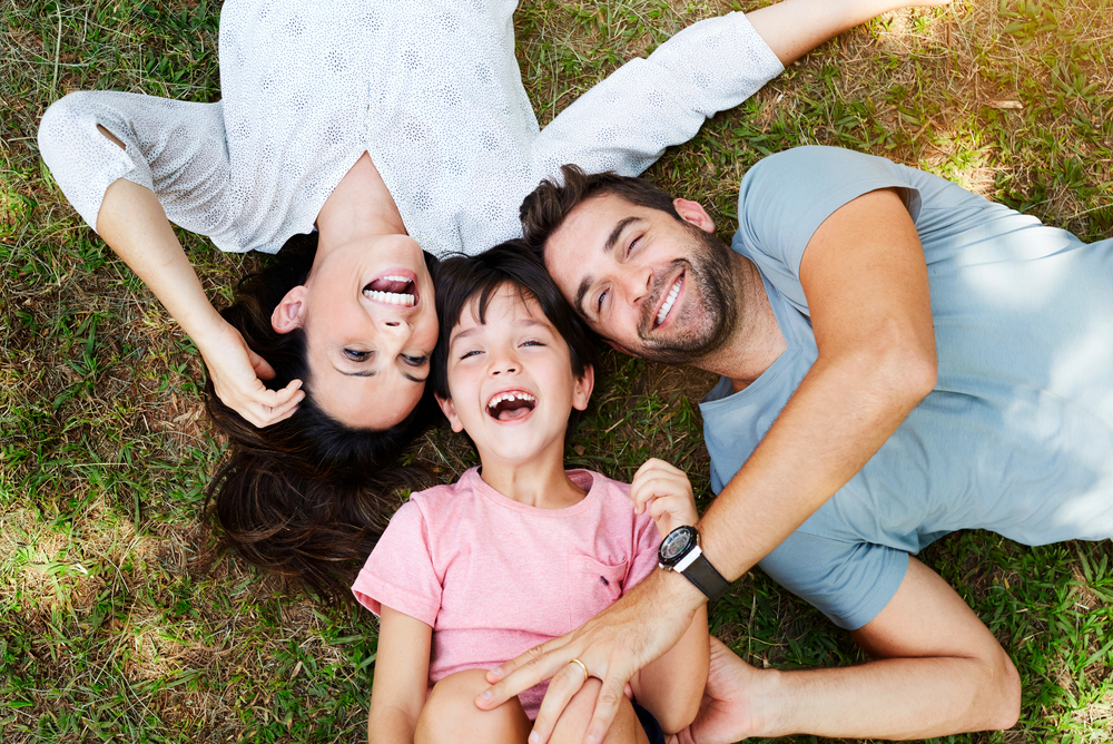 Dad, mom, child laying on grass with big smiles on sunny day