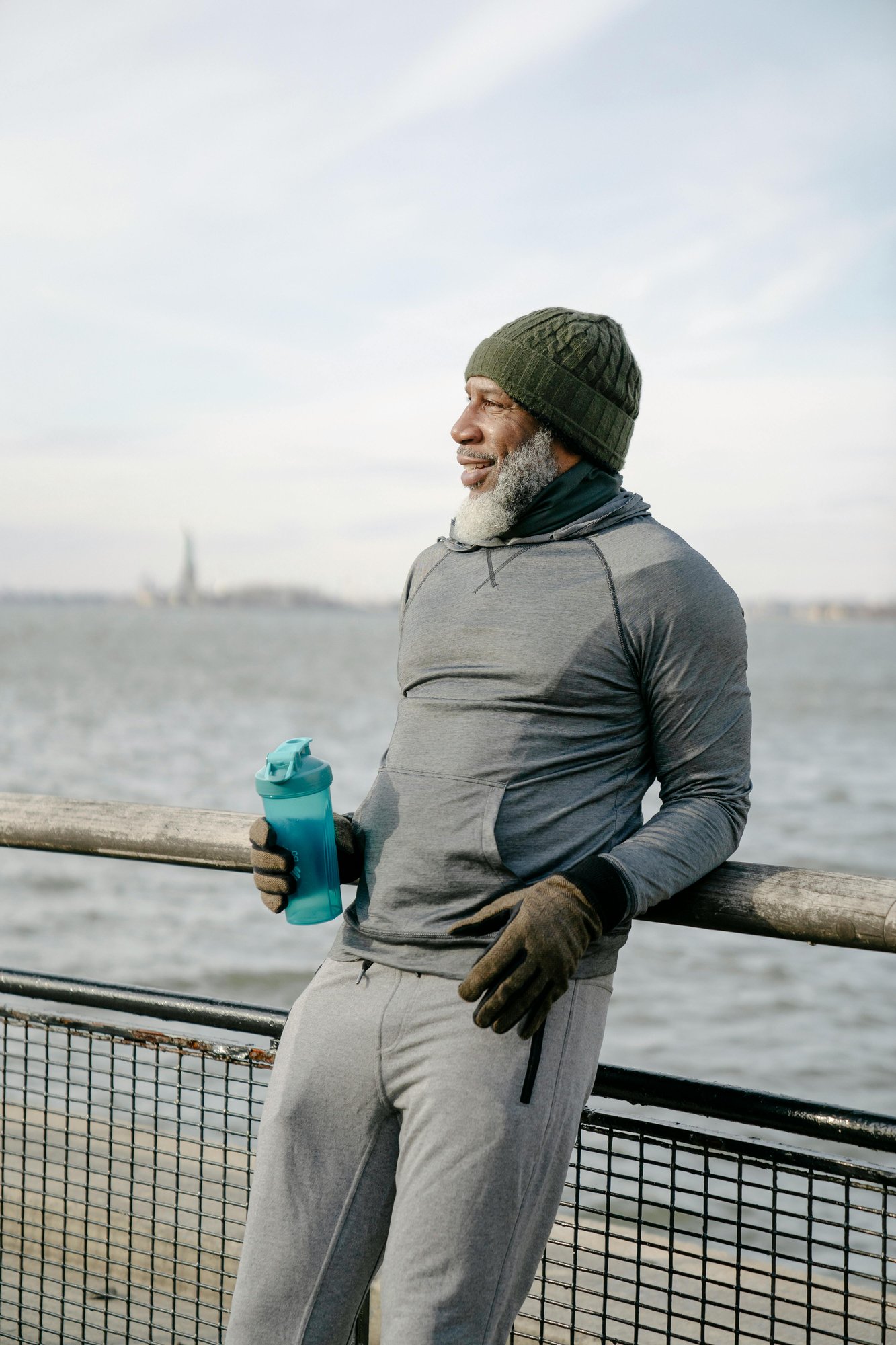 Jogger resting by the Hudson River in Brooklyn, dressed for cold weather, smiling.